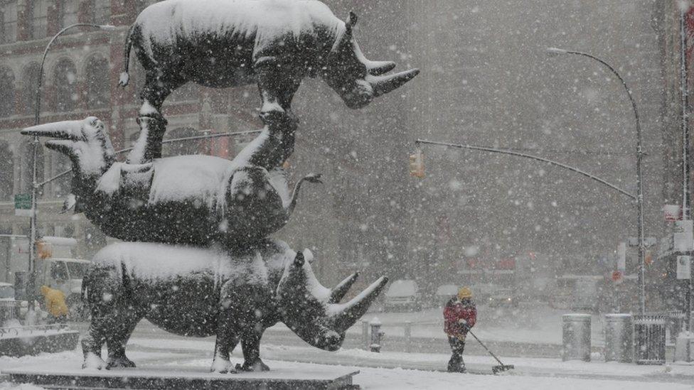 A worker clears snow near "The Last Three" sculpture in New York