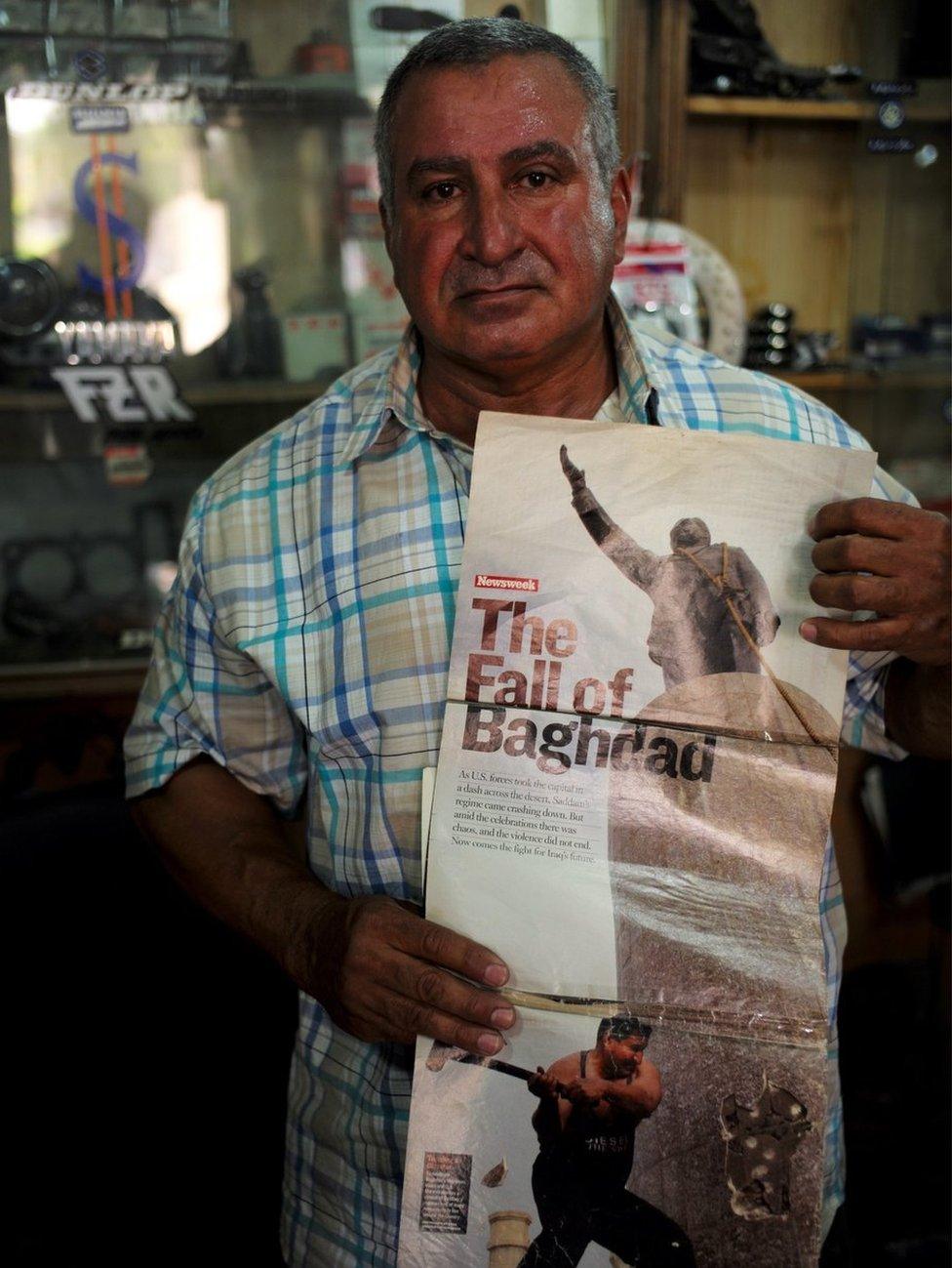 Kadhim holding a magazine photo from 13 years ago that showed him destroying the statue of Saddam Hussein