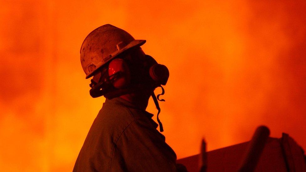 A worker wearing a respirator keeps an eye on molten steel at the TAMCO steel mini mill