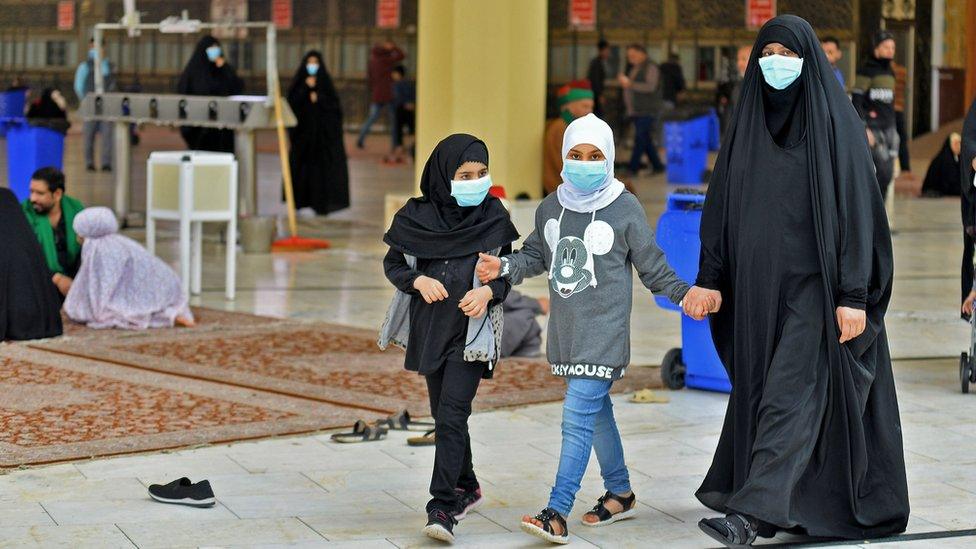 Two children and a woman wear face masks and hold hands