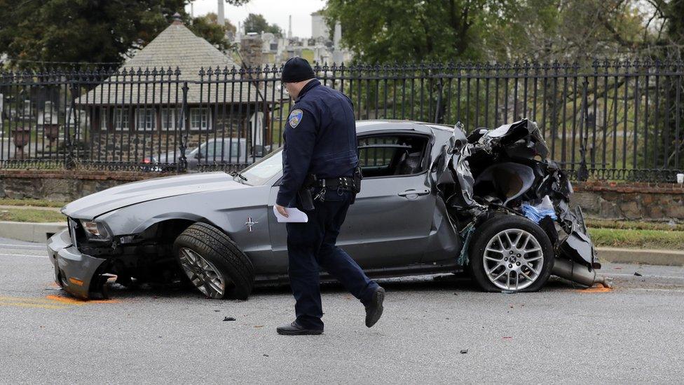 A member of the Baltimore Police Department walks past a car that was damaged by a school bus before the bus was involved in an early morning fatal collision