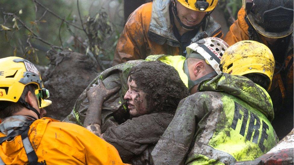 mud-covered woman being lifted by four emergency responders