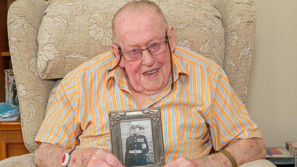 Bernard Botting holding a picture of himself as a marine.