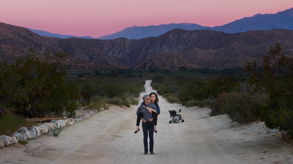 Omar carries Jen on his back in a desert