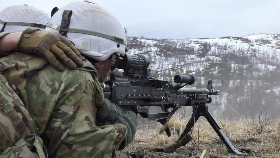 Two soldiers lie on the ground aiming down the sites of a machine gun in snowy environs