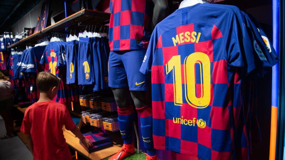 Child-stands-in-shop-next-to-row-of-Barcelona-shirts.