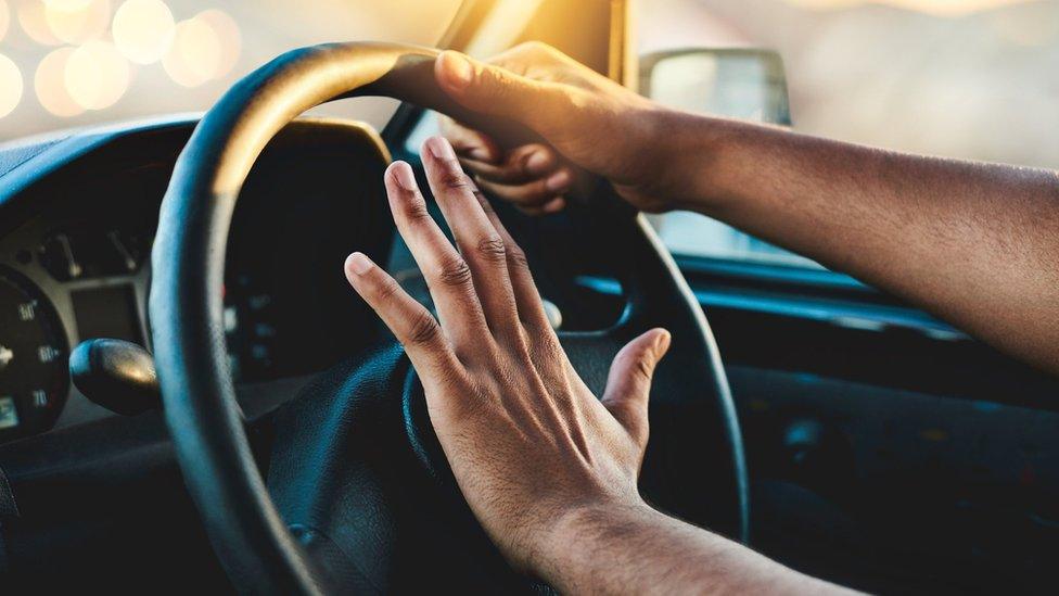 Hands on a steering wheel - one of them pressing the horn button in the middle
