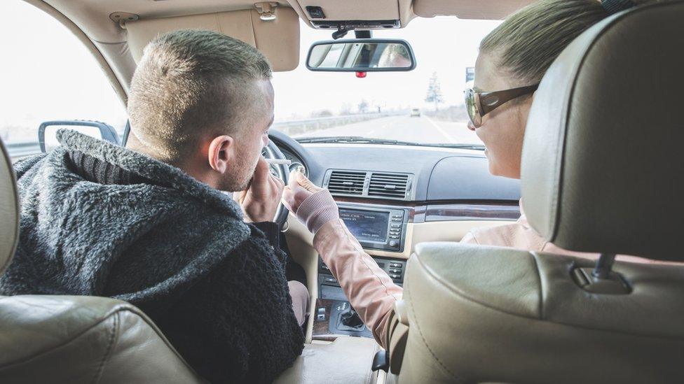 Couple traveling in car with man smoking a cigarette