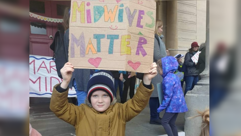 Child holds sign reading 'midwives matter'