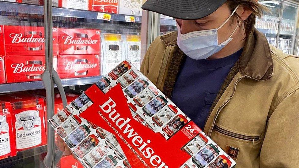 A man holding a case of Budweiser beers in a supermarket