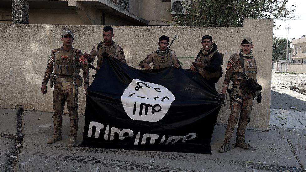 Troops hold an IS banner upside down in Qadsiya, Mosul