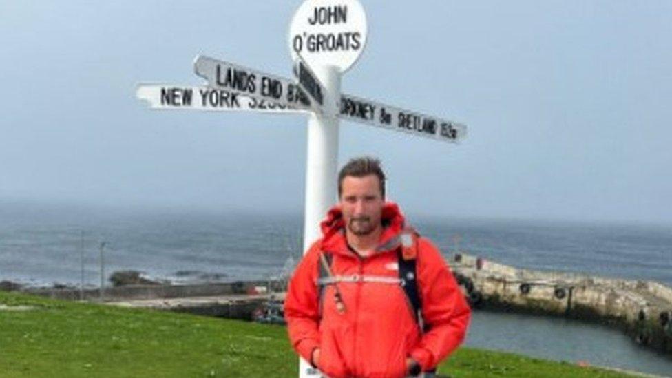 George Bromley stood in front of a signpost in John O'Groats