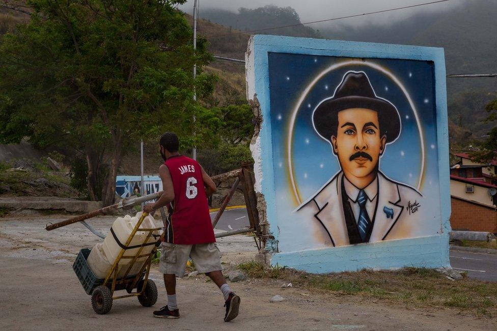 A man pushes a trolley by a mural of Jose Gregorio Hernandez, in Caracas