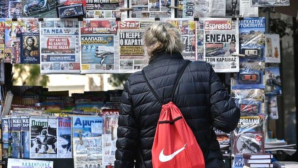 A woman reads newspaper's headlines referring to the killing of a Greek journalist in Athens on April 10, 2021.