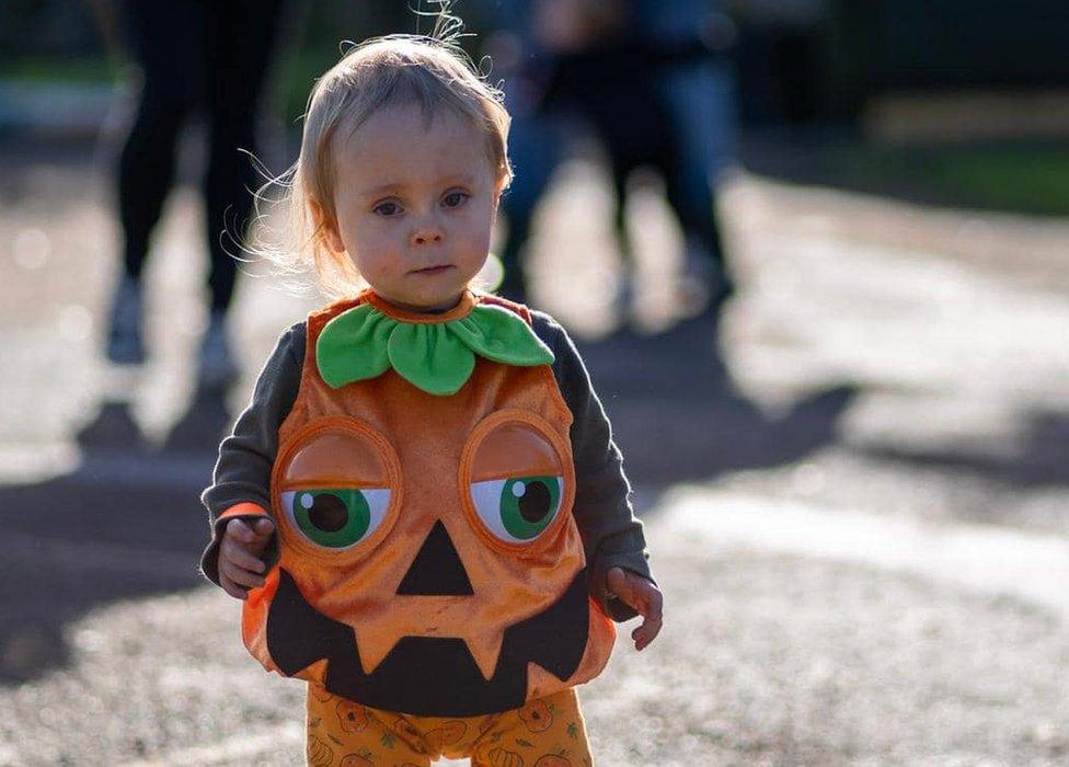 A toddler walking, wearing a pumpkin costume