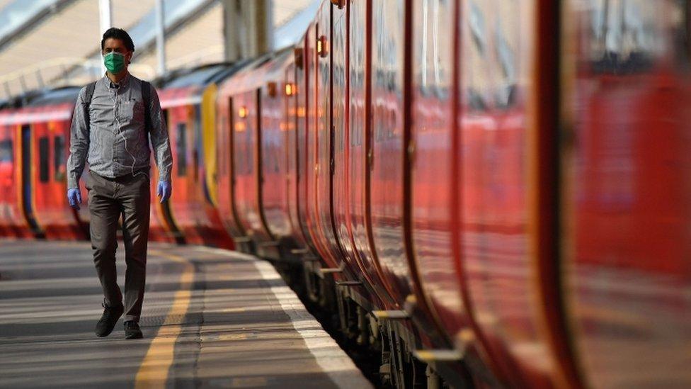 A man walks by trains wearing a mask