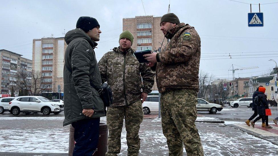 Conscription officers speak to a man on a street in Cherkasy