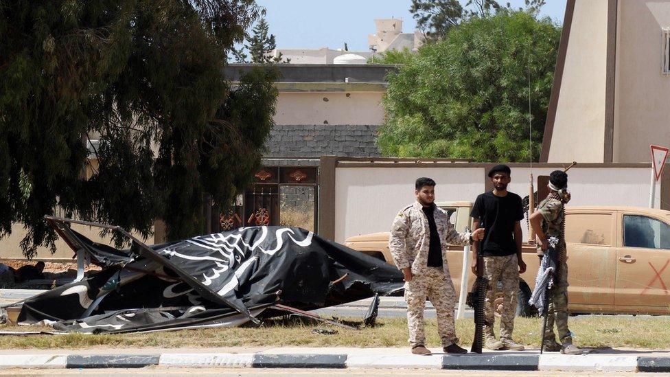 Forces loyal to Libya's UN-backed unity government stand next to an Islamic State group flag in Sirte's centre in June 2016