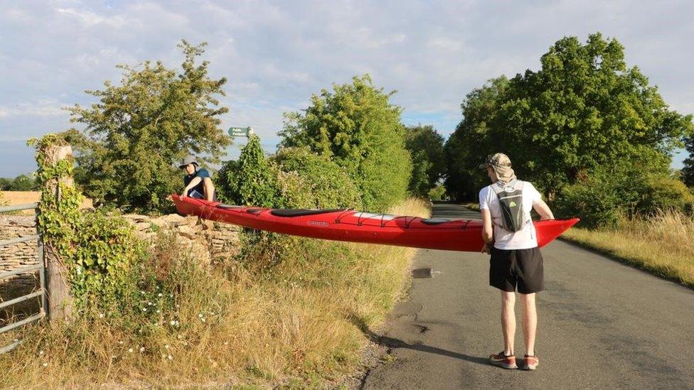 Two men lifting a red kayak over a wall on a country road