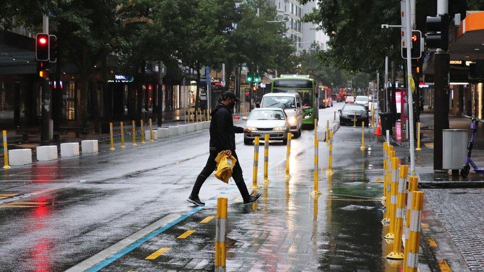 A man in a face mask crosses Queen Street in the early morning rain on February 15, 2021 in Auckland, New Zealand.