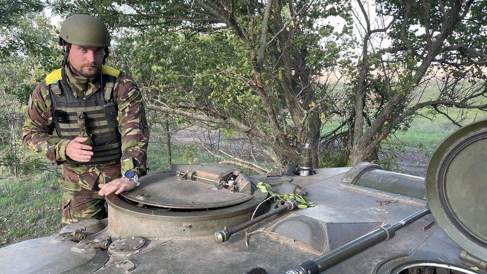 Stus, commander of the gunners standing next to a tank