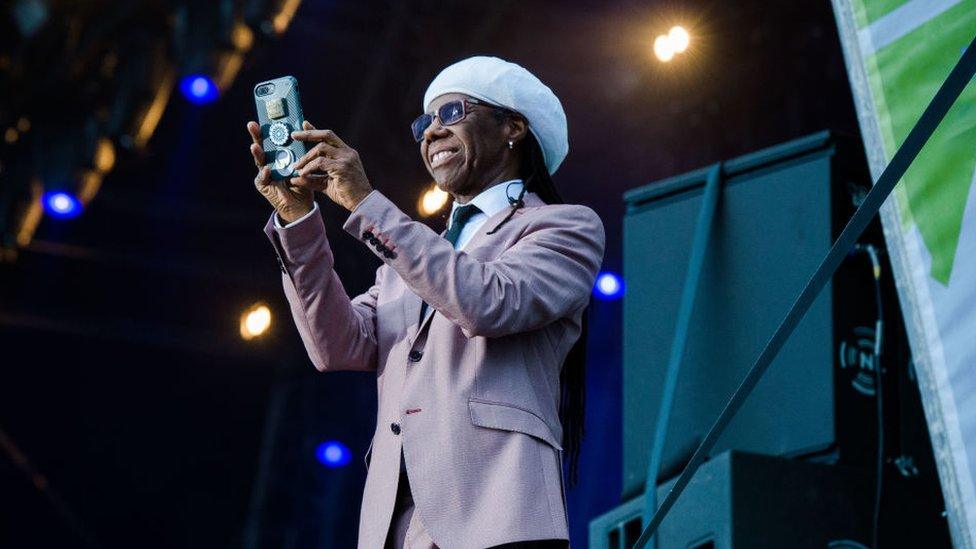 Nile Rodgers from Chic on stage at Belsonic in 2018, holding up his phone to take a picture of the audience