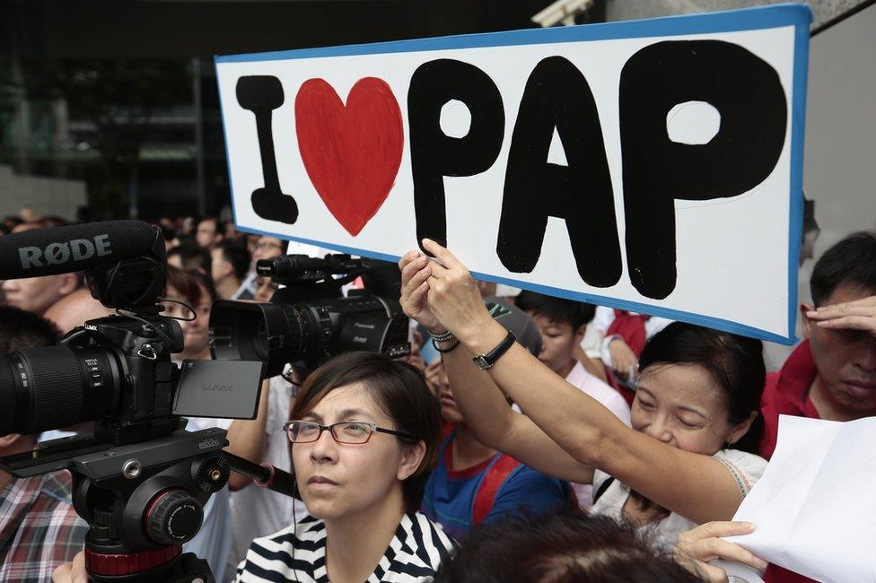 A supporter of the ruling People"s Action Party (PAP) holds up a placard during a lunchtime rally in the financial district of Singapore, 8 September 2015