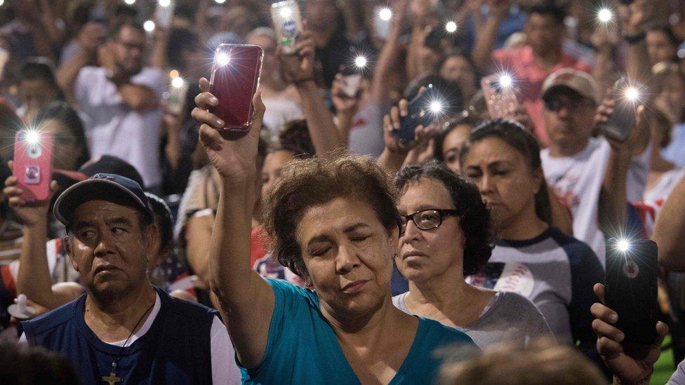 People hold up their phones during a prayer and candle vigil organized by the city, after a shooting left 20 people dead at the Cielo Vista Mall Wal-Mart in El Paso, Texas, on August 4, 2019.