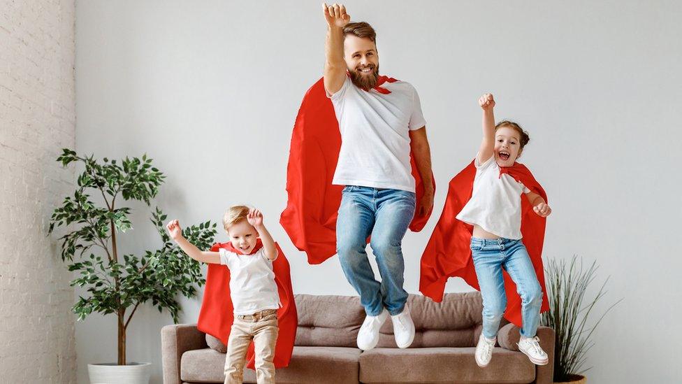 dad and two children jump in air with superhero capes