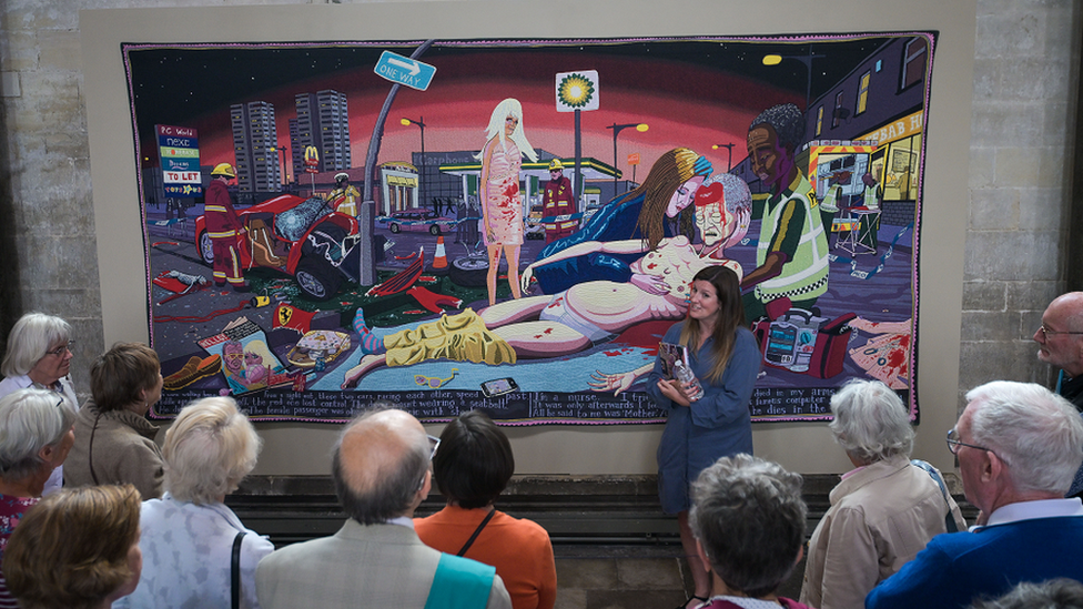 A woman presenting a large tapestry to a group of cathedral visitors