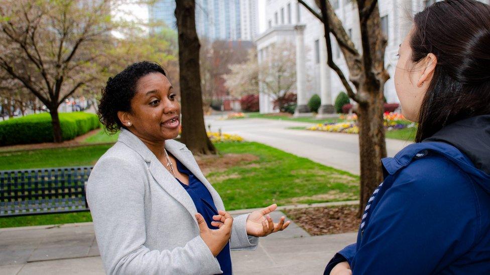 Chandra Farley is shown wearing a blazer and speaking to a woman she is standing across from,