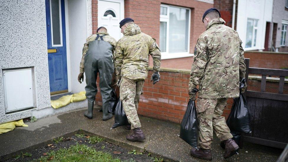 Three soldiers carrying sandbags to a house