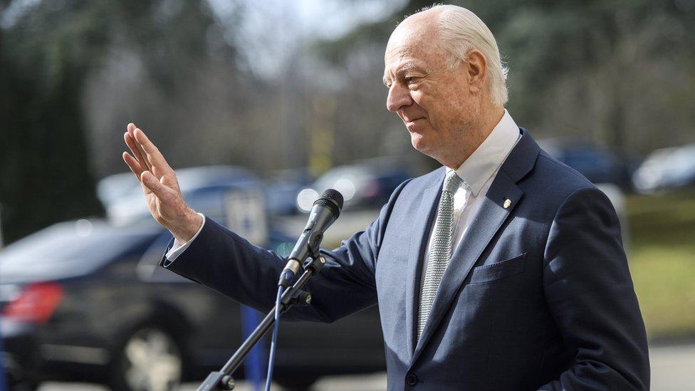 Staffan de Mistura, seen holding a hand up, palm open, standing before a microphone at a press event