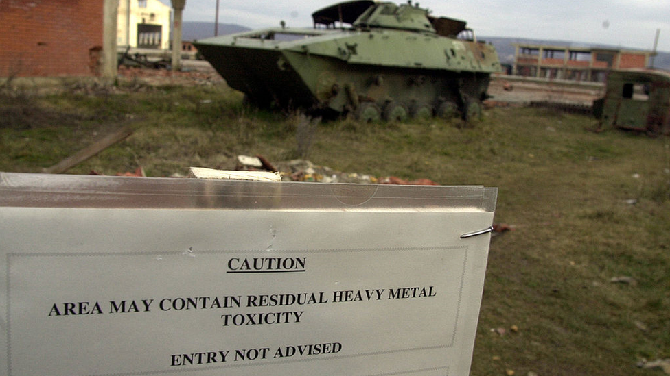 Destroyed armoured vehicles in Kosovo, 1999, and sign warning of heavy metal toxicity