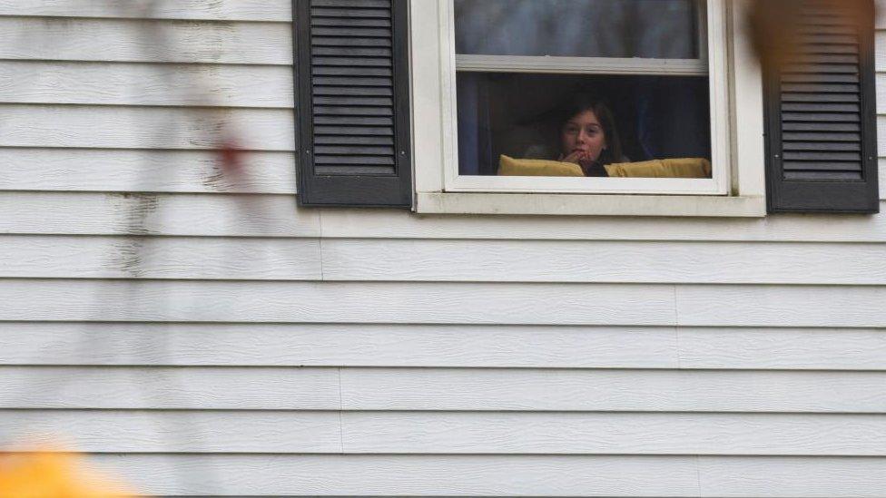 A child looks out through a window as Lisbon Falls remains on lockdown, following a deadly mass shooting in Lewiston, in Lisbon Falls, Maine,