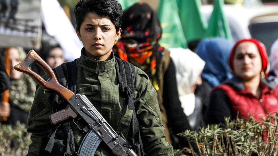 A Syrian Kurdish woman fighter stands as others march past during a demonstration in the north-eastern Syrian city of Qamishli as they mark the International Day for the Elimination of Violence against Women