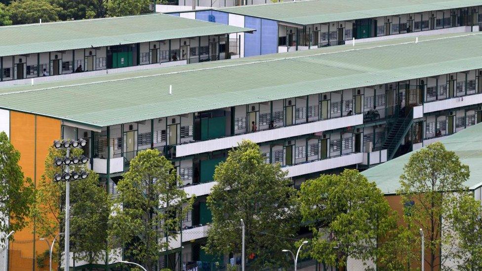 Men stand along a balcony of a dormitory used by foreign workers at Cochrane Lodge 2