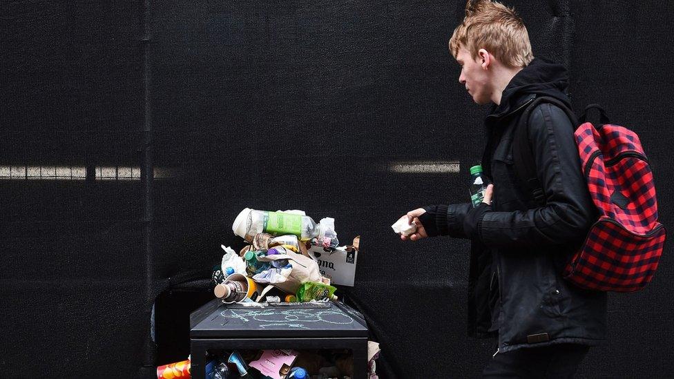 rubbish bin piled high with rubbish as a man walks past