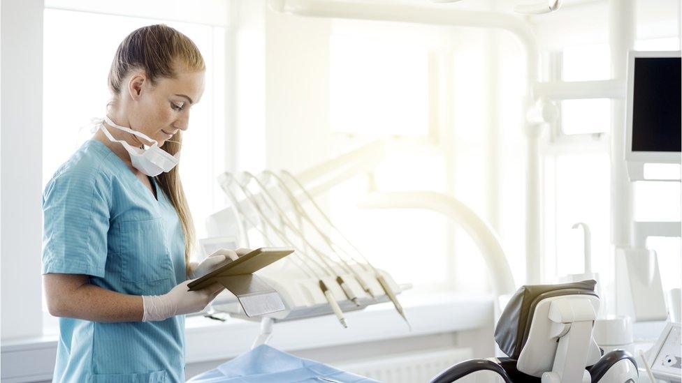 A dentist looks at an ipad next to the dentist chair