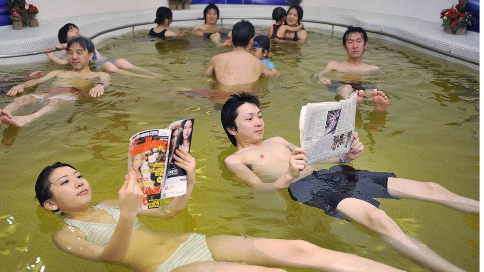 Two Japanese people read a magazine and a newspaper while floating in a "dead sea spa"