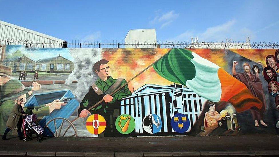 A woman with a pushchair walks past murals on the Falls road in west Belfas