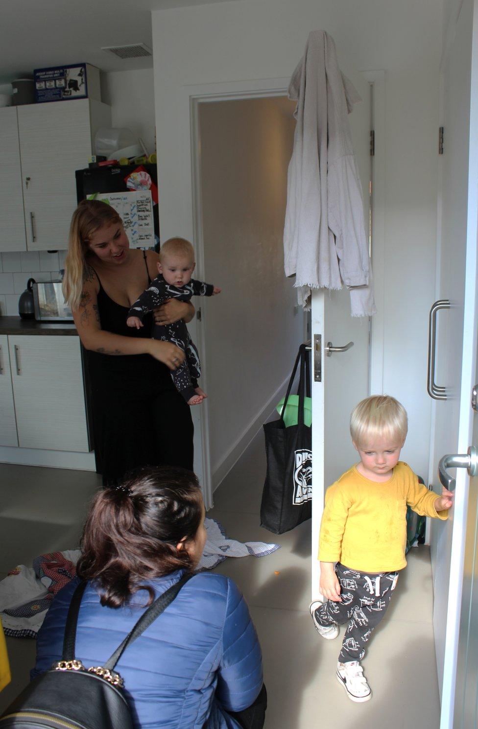 A woman crouches down to greet a little boy