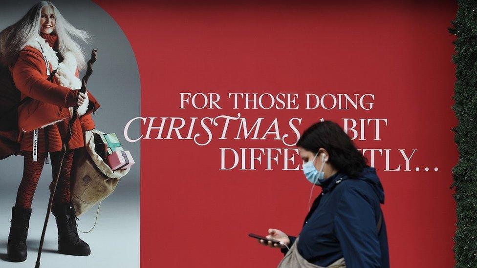 Woman wearing mask walking past Christmas poster