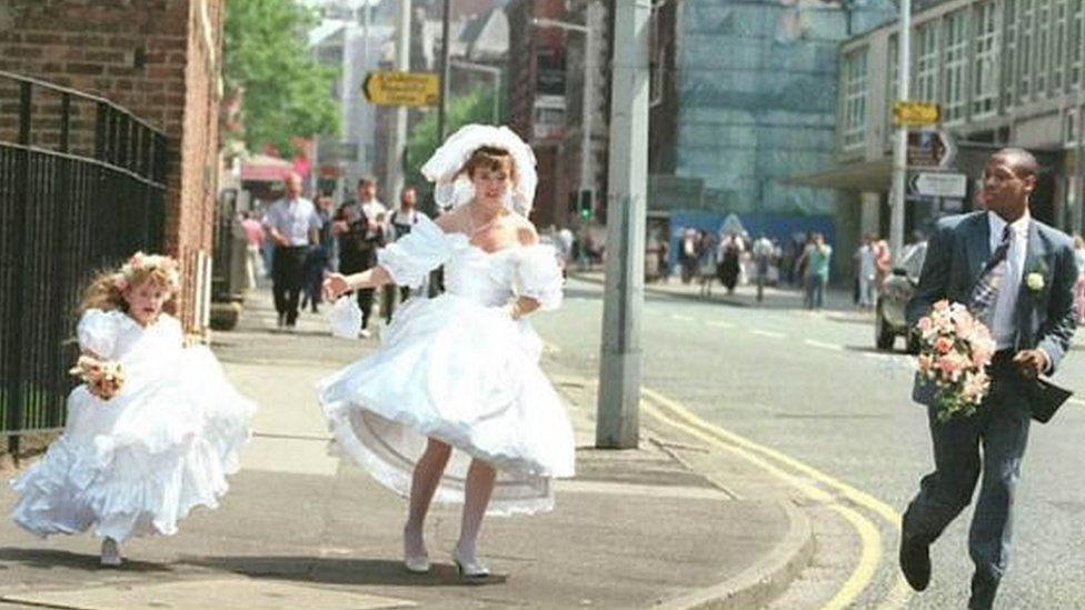 A bride and groom and their bridesmaid fleeing through the city centre