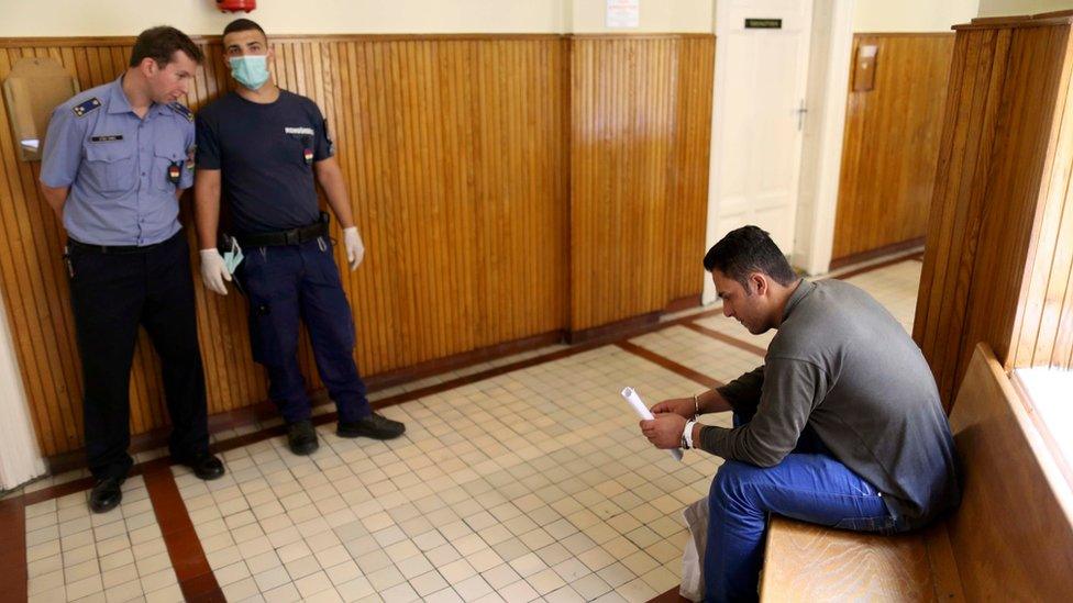 A migrant is guarded by policemen as he waits to appear in front of a court in Szeged, Hungary, on 16 September 2015