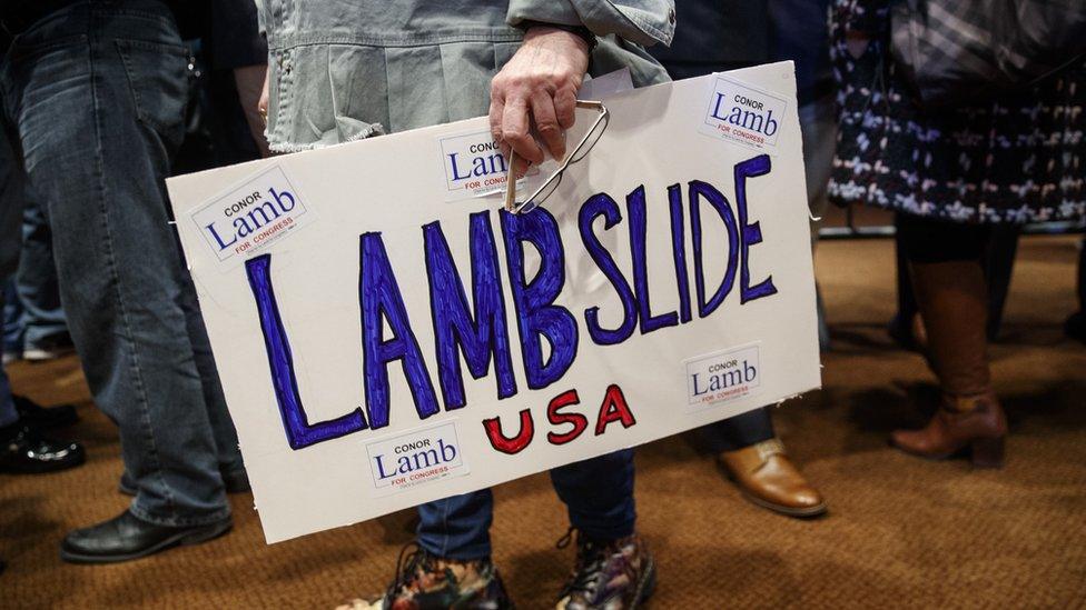 A man holds a "Lambslide" sign.