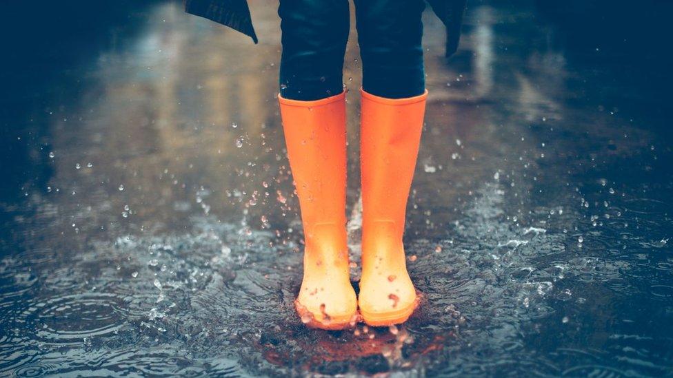 Close-up of woman in orange rubber boots jumping on the puddle