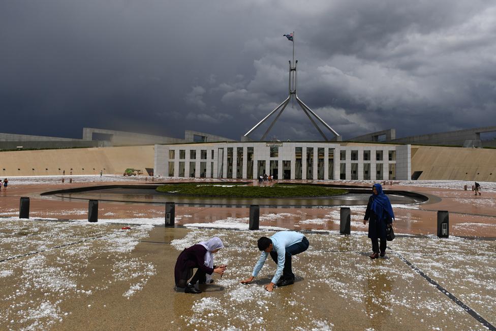 People look at hail stones on the ground after a severe hail storm at Parliament House