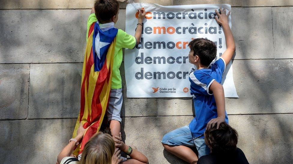 boys climbing on people's heads to affix a poster reading "democracia" to a wall