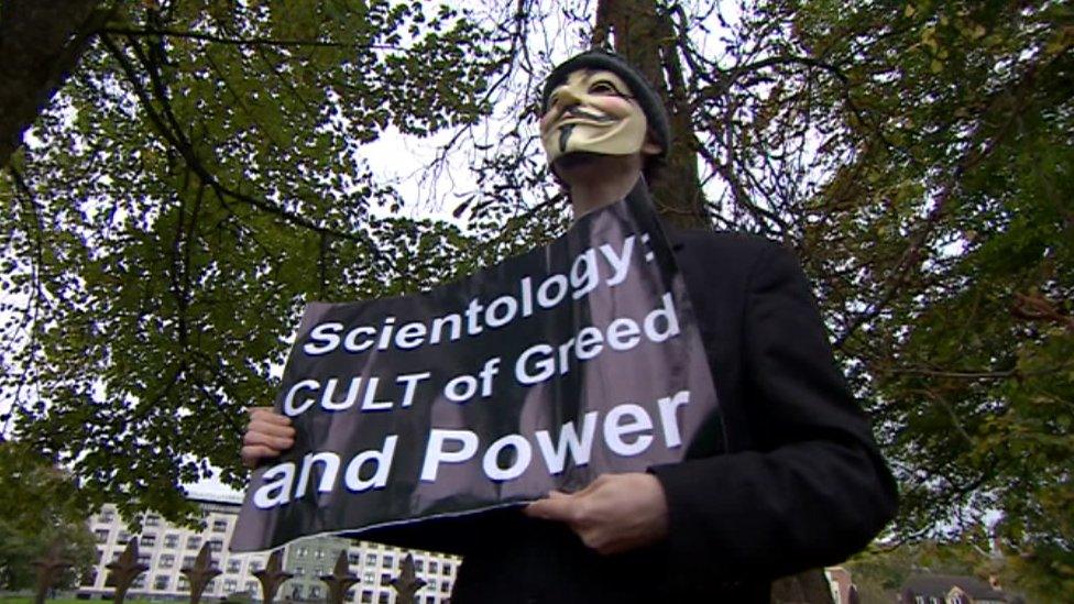 A protester holds a sign reading "Scientology: Cult of greed and power"